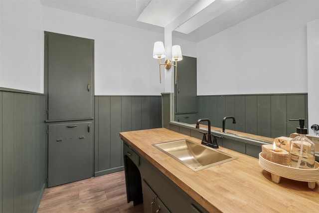 kitchen with a sink, wood finished floors, a wainscoted wall, and wood counters