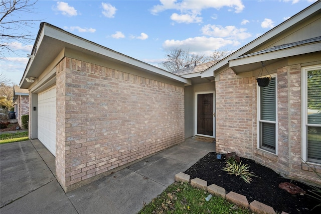 property entrance with brick siding, an attached garage, and concrete driveway