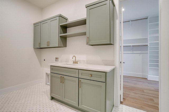 kitchen with baseboards, open shelves, a sink, light countertops, and green cabinets