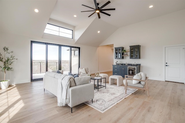 living area featuring light wood-type flooring, high vaulted ceiling, indoor wet bar, baseboards, and ceiling fan