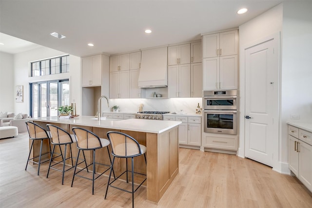 kitchen featuring a sink, light wood-type flooring, premium range hood, and stainless steel appliances