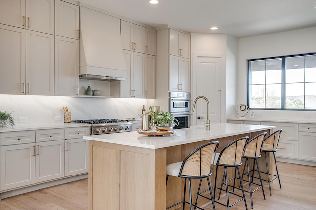 kitchen featuring light wood finished floors, a breakfast bar area, light countertops, and premium range hood