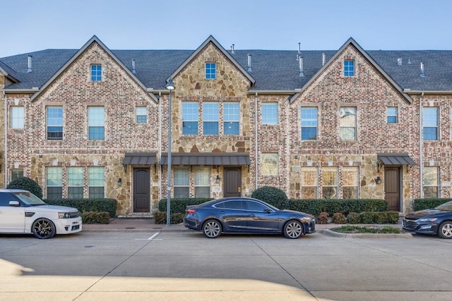 townhome / multi-family property with brick siding, stone siding, and roof with shingles