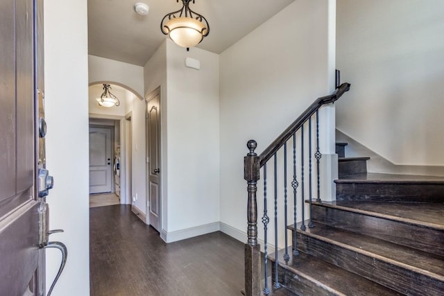 entrance foyer with arched walkways, stairway, dark wood finished floors, and baseboards