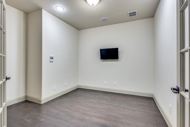 empty room with dark wood-style floors, visible vents, and baseboards