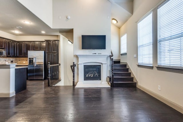 living area with baseboards, stairway, a glass covered fireplace, high vaulted ceiling, and dark wood-style flooring