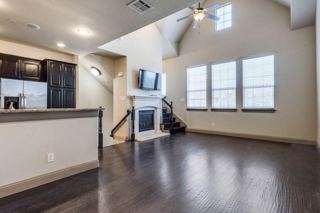 unfurnished living room featuring visible vents, dark wood-style flooring, a ceiling fan, and a glass covered fireplace