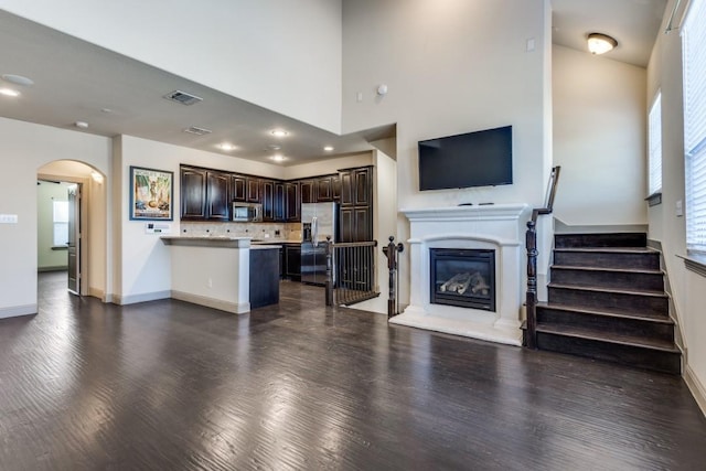 living area with stairway, baseboards, visible vents, dark wood-style flooring, and a glass covered fireplace