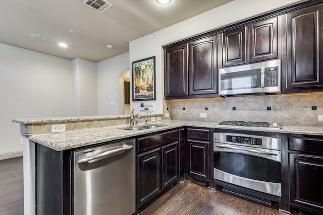 kitchen featuring visible vents, a sink, a peninsula, stainless steel appliances, and dark wood-style flooring