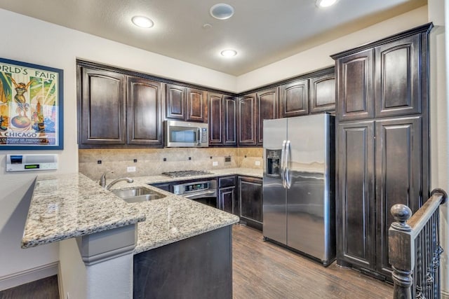 kitchen featuring light stone countertops, a peninsula, a sink, stainless steel appliances, and dark brown cabinets