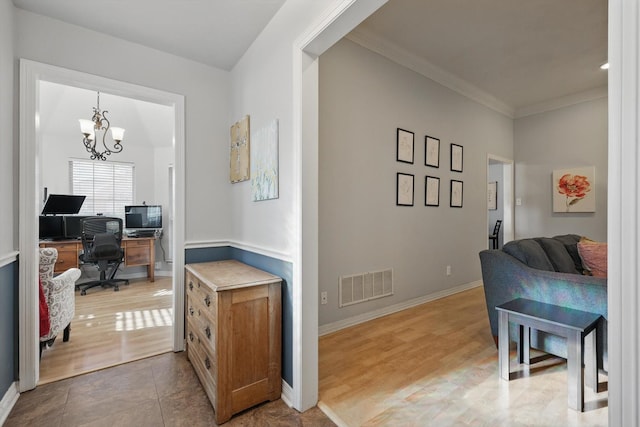 corridor featuring visible vents, a notable chandelier, crown molding, light wood finished floors, and baseboards