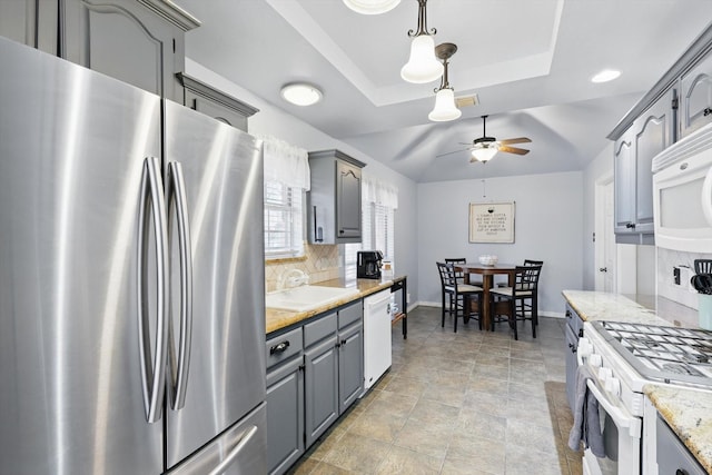 kitchen featuring backsplash, gray cabinetry, white appliances, a raised ceiling, and a sink