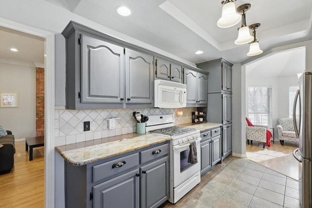 kitchen featuring white appliances, light stone countertops, a tray ceiling, gray cabinets, and decorative backsplash