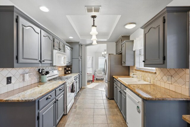 kitchen featuring visible vents, gray cabinets, a sink, white appliances, and a raised ceiling