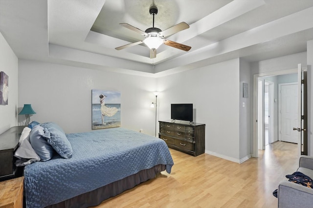 bedroom featuring baseboards, a raised ceiling, wood finished floors, and a ceiling fan