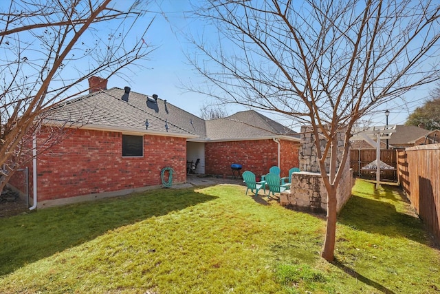 back of property with brick siding, roof with shingles, a lawn, a chimney, and a fenced backyard