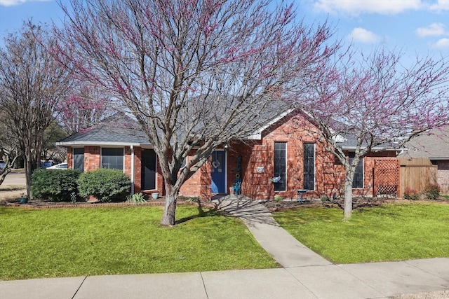 view of front of home featuring a front yard, brick siding, and roof with shingles