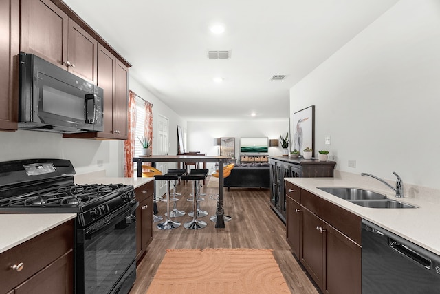 kitchen with a sink, black appliances, light countertops, dark wood-type flooring, and dark brown cabinetry