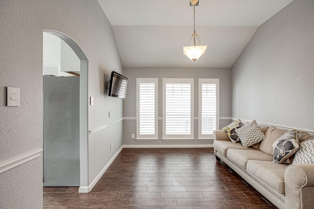 living area with baseboards, wood finish floors, arched walkways, vaulted ceiling, and a textured wall