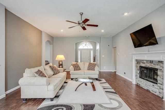 living room with wood finished floors, baseboards, recessed lighting, arched walkways, and a stone fireplace