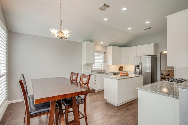 kitchen with visible vents, a kitchen island, appliances with stainless steel finishes, wood finished floors, and a sink