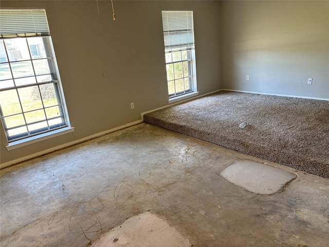 empty room with unfinished concrete floors, a healthy amount of sunlight, and baseboards