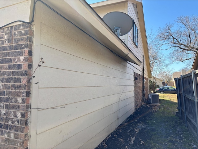 view of side of home featuring central air condition unit, fence, and brick siding