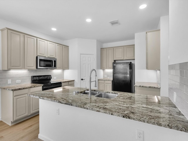 kitchen featuring visible vents, light wood-type flooring, black appliances, a sink, and light stone counters