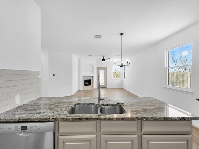 kitchen featuring visible vents, light stone counters, a fireplace, stainless steel dishwasher, and a sink