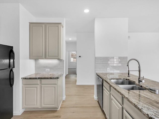 kitchen featuring stainless steel dishwasher, light stone countertops, freestanding refrigerator, and a sink