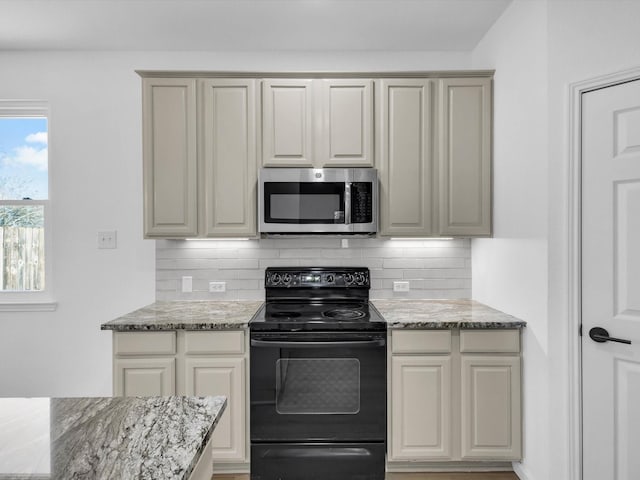 kitchen featuring stainless steel microwave, light stone counters, black electric range oven, and backsplash