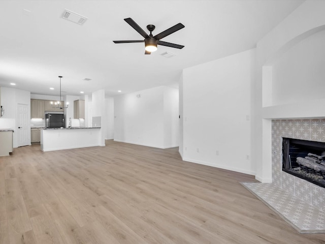 unfurnished living room with visible vents, ceiling fan with notable chandelier, a fireplace, and light wood finished floors