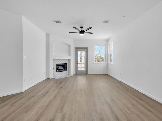 unfurnished living room featuring a ceiling fan, visible vents, light wood finished floors, baseboards, and a tiled fireplace