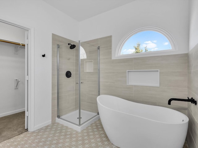 full bathroom with a walk in closet, tile walls, a freestanding tub, and a stall shower