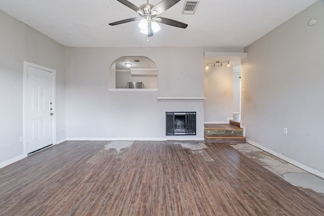 unfurnished living room featuring wood finished floors, baseboards, visible vents, a fireplace with raised hearth, and a textured ceiling