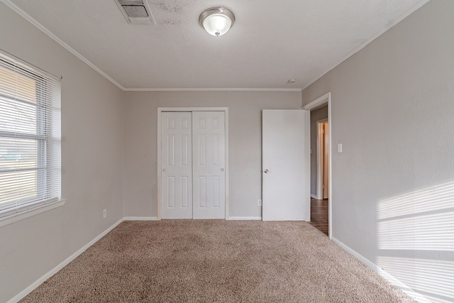 unfurnished bedroom featuring carpet flooring, visible vents, a closet, and ornamental molding