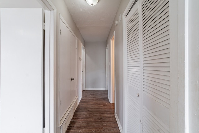 hall featuring baseboards, dark wood-type flooring, and a textured ceiling