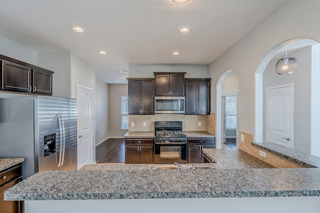 kitchen featuring dark brown cabinetry, decorative backsplash, appliances with stainless steel finishes, and wood finished floors