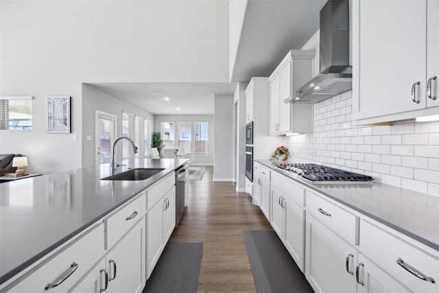 kitchen featuring a sink, dark wood-style floors, appliances with stainless steel finishes, wall chimney range hood, and decorative backsplash