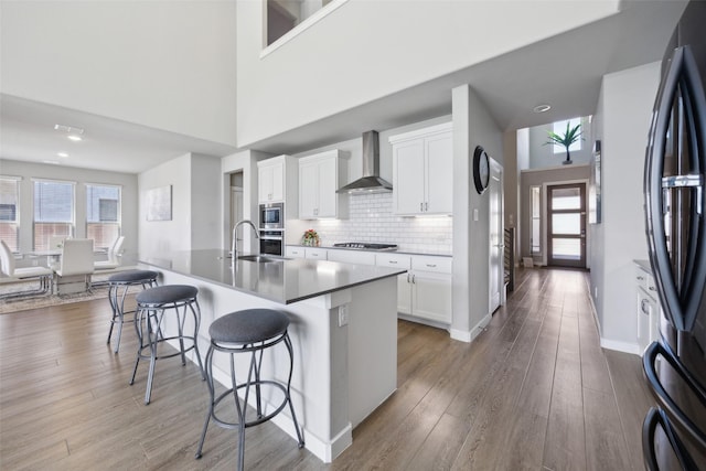 kitchen featuring wall chimney range hood, light wood-style flooring, stainless steel appliances, a kitchen breakfast bar, and tasteful backsplash