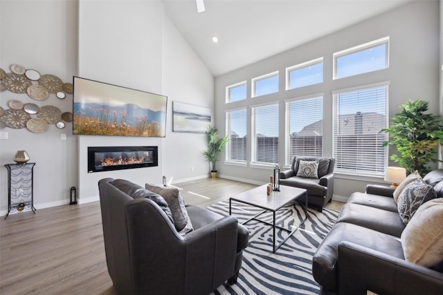 living area featuring a glass covered fireplace, plenty of natural light, high vaulted ceiling, and wood finished floors