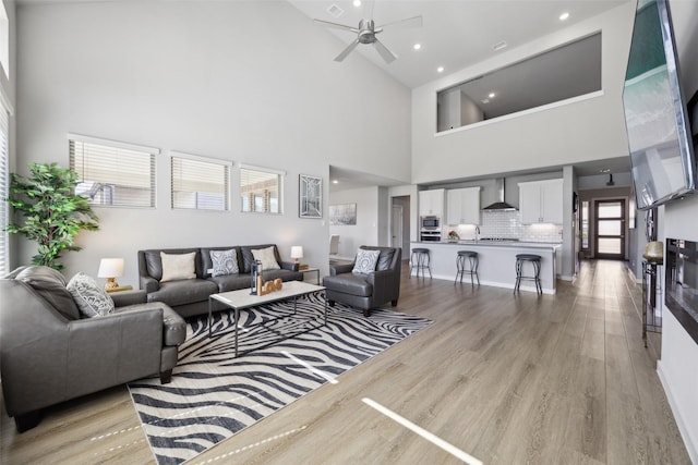 living room featuring light wood-type flooring, a high ceiling, and ceiling fan