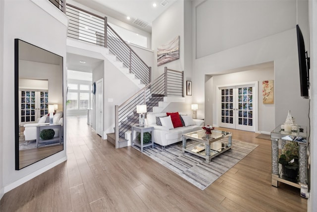 living room featuring stairway, wood finished floors, visible vents, french doors, and a towering ceiling