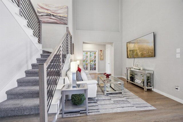 living room featuring wood finished floors, baseboards, a high ceiling, stairs, and french doors