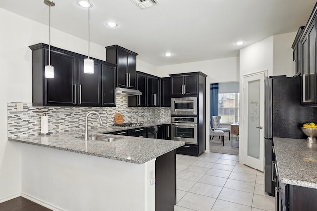 kitchen with visible vents, under cabinet range hood, a sink, appliances with stainless steel finishes, and a peninsula