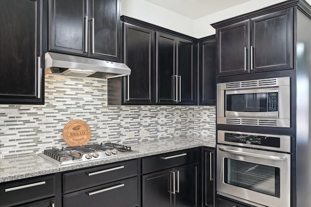 kitchen featuring under cabinet range hood, decorative backsplash, dark cabinetry, stainless steel appliances, and a warming drawer