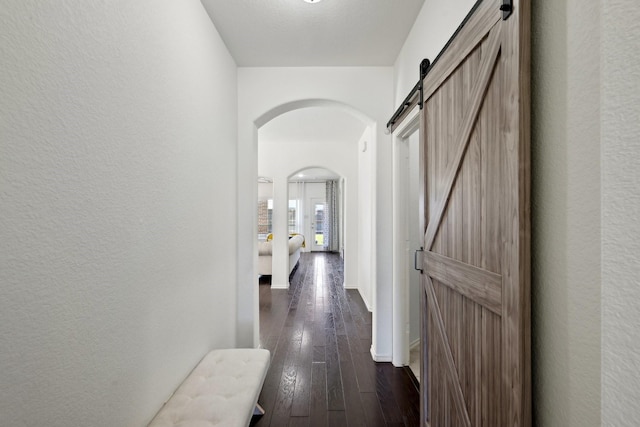 corridor featuring dark wood-style floors, baseboards, a barn door, and a textured wall