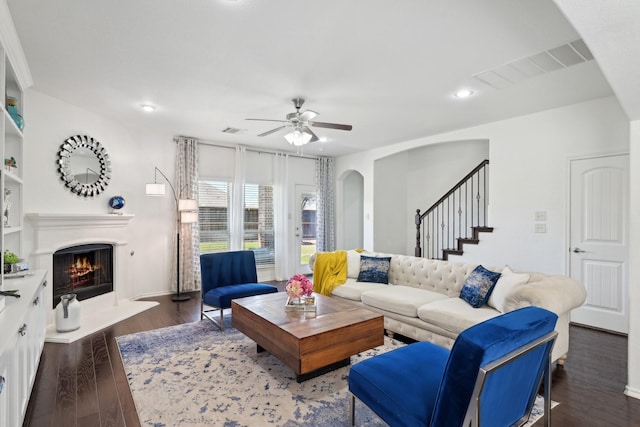 living room with dark wood-style floors, visible vents, ceiling fan, and a lit fireplace