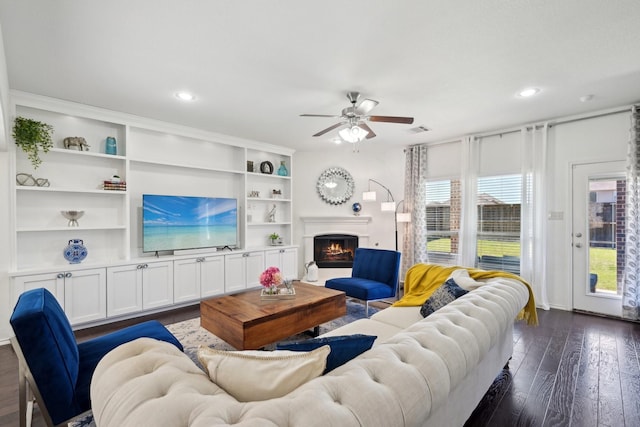 living area with a ceiling fan, visible vents, recessed lighting, a warm lit fireplace, and dark wood-type flooring