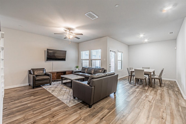 living room with visible vents, light wood-style flooring, a ceiling fan, and baseboards